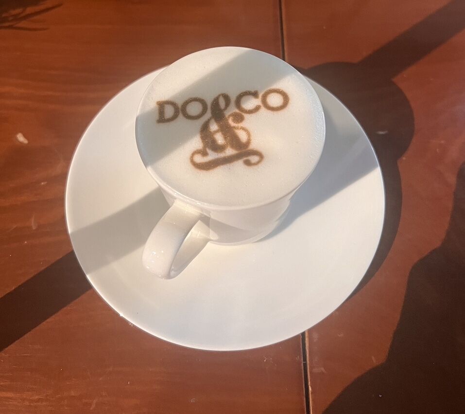 Kaffeeservice 4 A Cup Of Coffee With A Custom Logo &Quot;Dooco&Quot; Printed On The Foam, Served On A White Saucer.